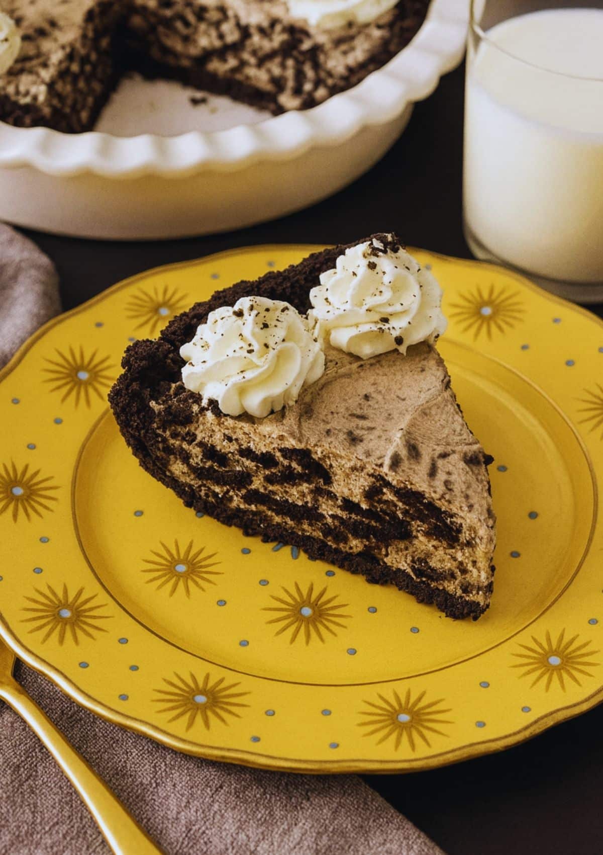 Slice of Oreo pie on a yellow plate decorated with golden sunbursts and blue dots