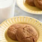 Chewy gingersnap cookies on a yellow dessert plate with a glass of milk
