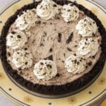 Whole Oreo pie with whipped cream swirls on a yellow plate decorated with golden sunbursts
