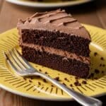 Slice of chocolate cake on yellow plate with golden sunburst rim